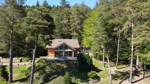 Una cabaña moderna con techo inclinado, rodeada de un bosque denso.