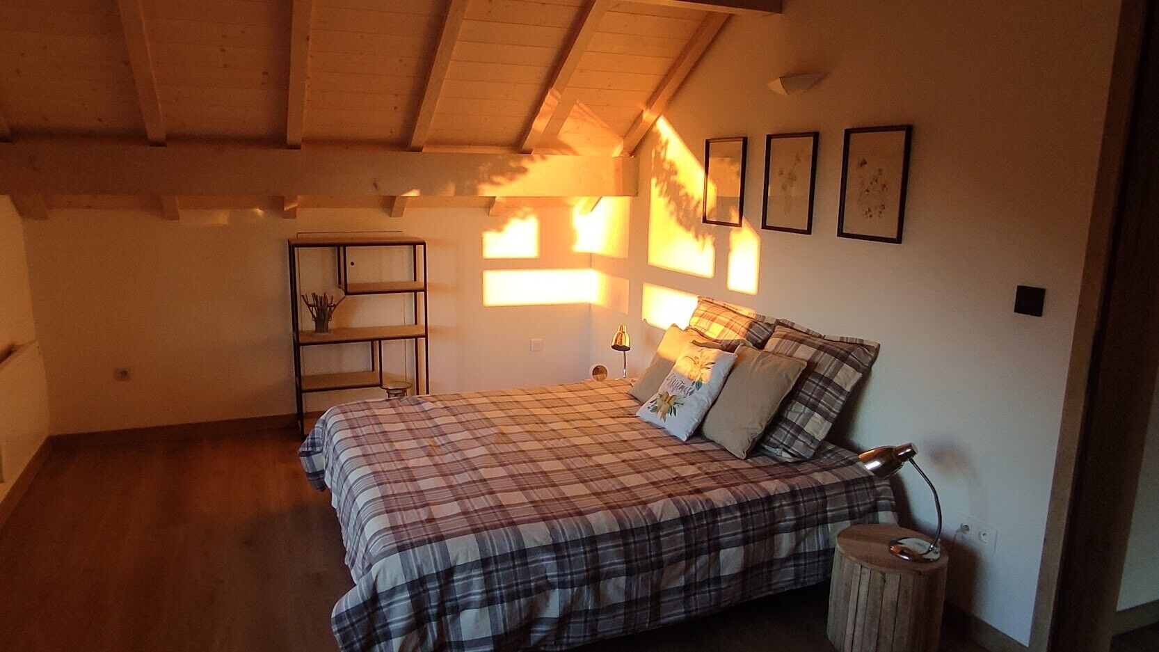A bedroom with a bed, bedside lamps, a shelf, and framed pictures on the wall.
