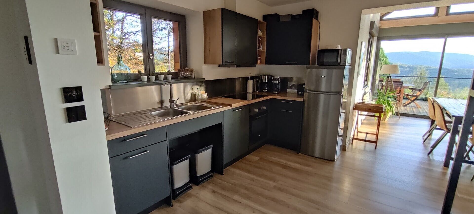 Ett modernt kök med ett kylskåp i rostfritt stål, en diskho och en kaffebryggare. Det finns ett fönster med utsikt över omgivningen.