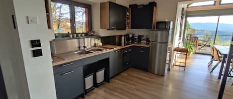 A modern kitchen with a stainless steel refrigerator, a sink, and a coffee maker. There is a window with a view of the outdoors.