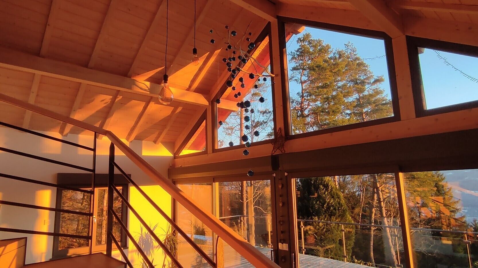 A wooden interior with a staircase, large windows, and a view of trees.