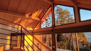 Interior de madera con una escalera, ventanas amplias y vista a árboles.