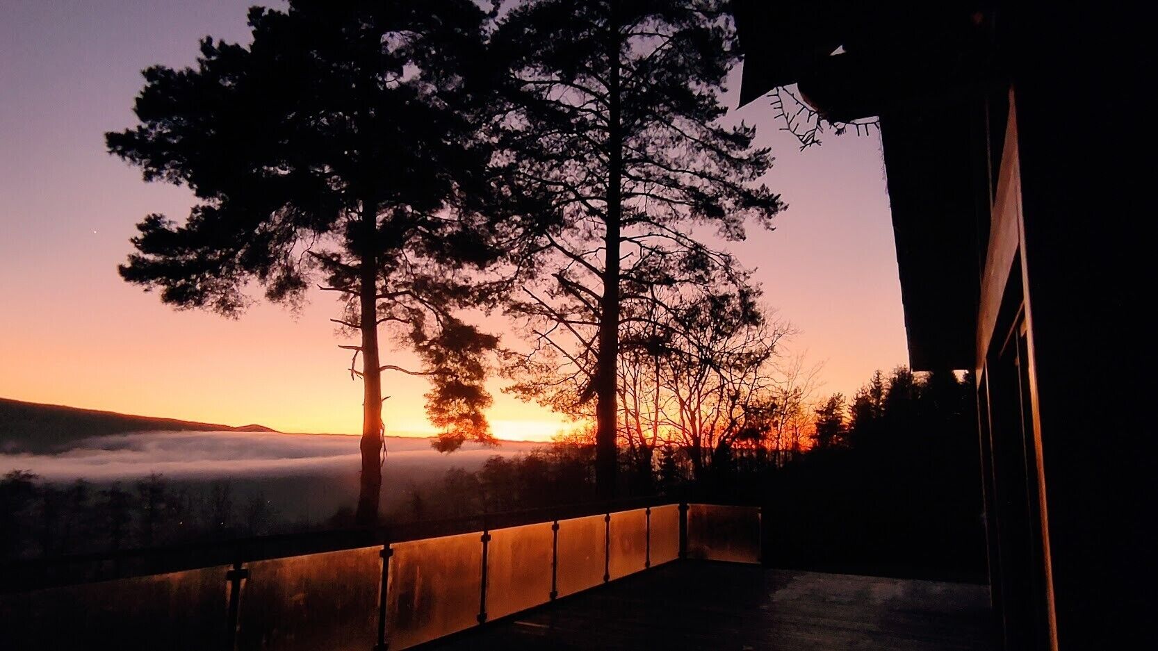 Une vue sur le coucher de soleil depuis un balcon, avec des arbres et une balustrade.