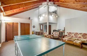 Een kamer met een tafeltennistafel, houten meubels, een bank en een plafondventilator.