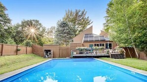 Ein Garten mit Schwimmbad, einer Holzterrasse und einem Haus mit Solaranlage.
