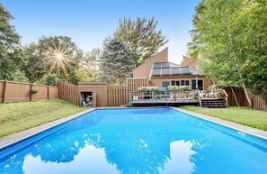 A backyard with a swimming pool, a wooden deck, and a house with solar panels. - Peaceful 1-bedroom condo in charming Waitsfield awaits you (Waitsfield)