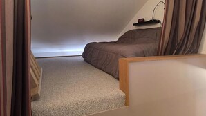 Ein Schlafzimmer mit schrägem Dach, einem Bett, einem Nachttisch und einem kleinen Regal mit einer Uhr.