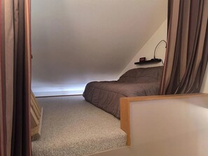 A bedroom with a sloped ceiling, a bed, a bedside table, and a small shelf with a clock. - Peaceful 1-bedroom condo in charming Waitsfield awaits you (Waitsfield)