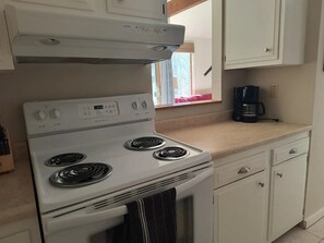 A kitchen with a white stove, a coffee maker, and cabinets. - Peaceful 1-bedroom condo in charming Waitsfield awaits you (Waitsfield)
