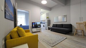 A living room with a sofa, a television, a washing machine, and a dining area. - KYANA Luxury KVA (Kavala)