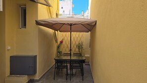 Eine schmale Außenpatio mit Tisch und Stühlen, einem Sonnenschirm und einem an der Wand befestigten Schrank.
