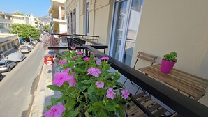A balcony with a view of parked cars and a street, a wooden bench, and a potted plant. - KYANA Luxury KVA (Kavala)