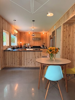 Una cocina moderna con paneles de madera, una zona de comedor con una mesa redonda y sillas, y vistas al exterior a través de amplios ventanales.