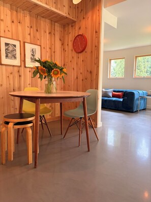 Un comedor con una mesa y sillas de madera, un jarrón con girasoles y un reloj rojo en la pared.