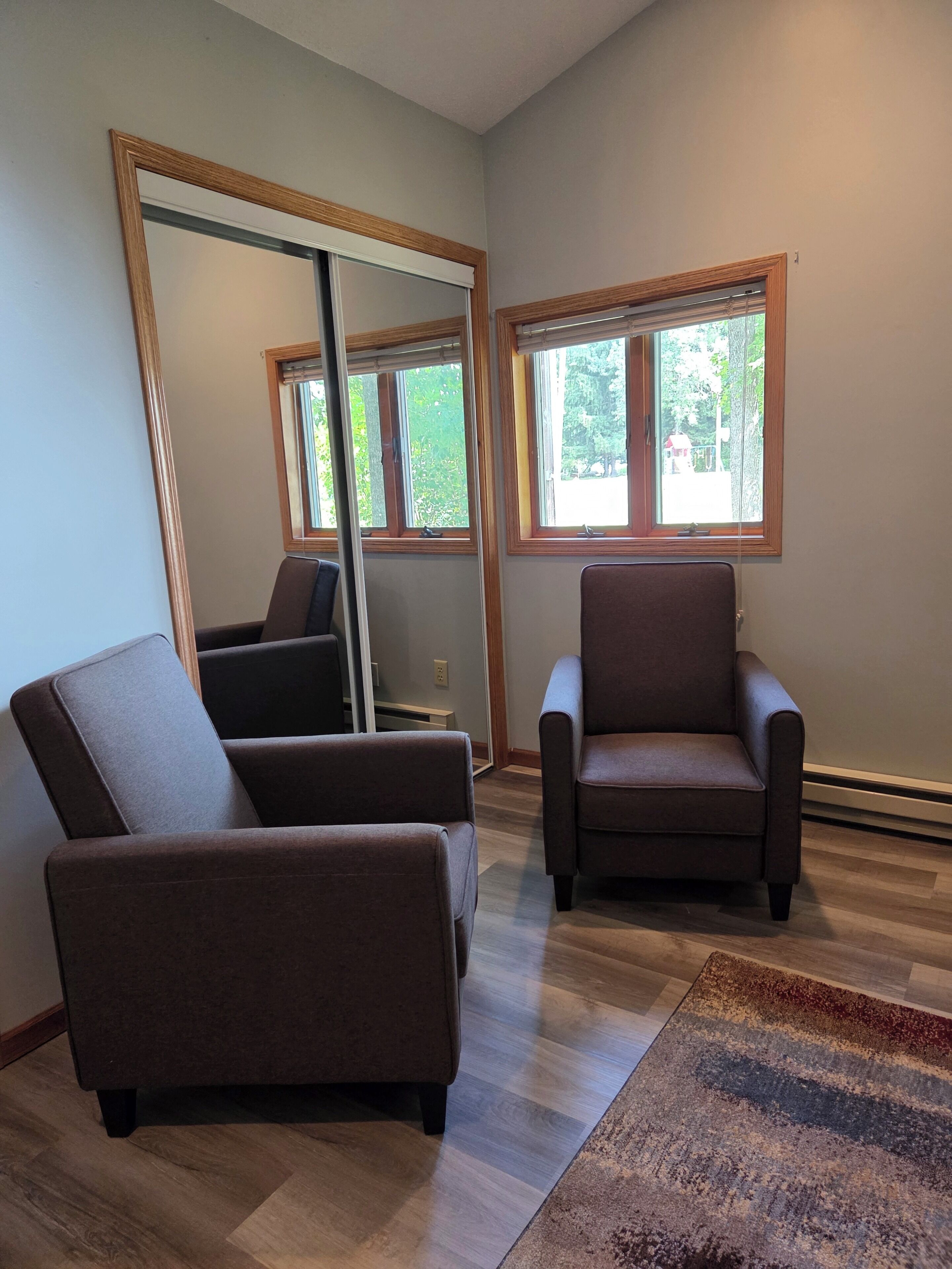 A room with two armchairs, a large mirror, and a view of the outdoors through windows.