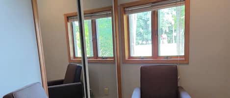 A room with two armchairs, a large mirror, and a view of the outdoors through windows.