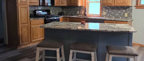 A kitchen with wooden cabinets, a granite countertop, and a central island with stools.