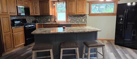 A kitchen with wooden cabinets, a black refrigerator, a stove, and a large island with stools.