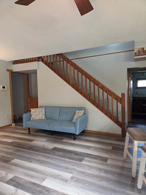 A living room with a blue sofa, wooden staircase, and a dining area with a bench. - Spacious home with extra lofts, near Duluth with Jay Cooke State Park steps away (Carlton)