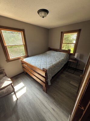 A bedroom with a wooden bed, two windows, a ceiling light, and a small table with a lamp. - Rush Lake Retreat -plenty of room to sleep, even more room to unwind! (Rush City)