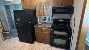 Una cocina compacta con armarios de madera, un refrigerador negro, un microondas y un horno.