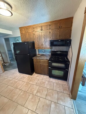 A compact kitchen with wooden cabinets, a black refrigerator, a microwave, and an oven. - Rush Lake Retreat -plenty of room to sleep, even more room to unwind! (Rush City)