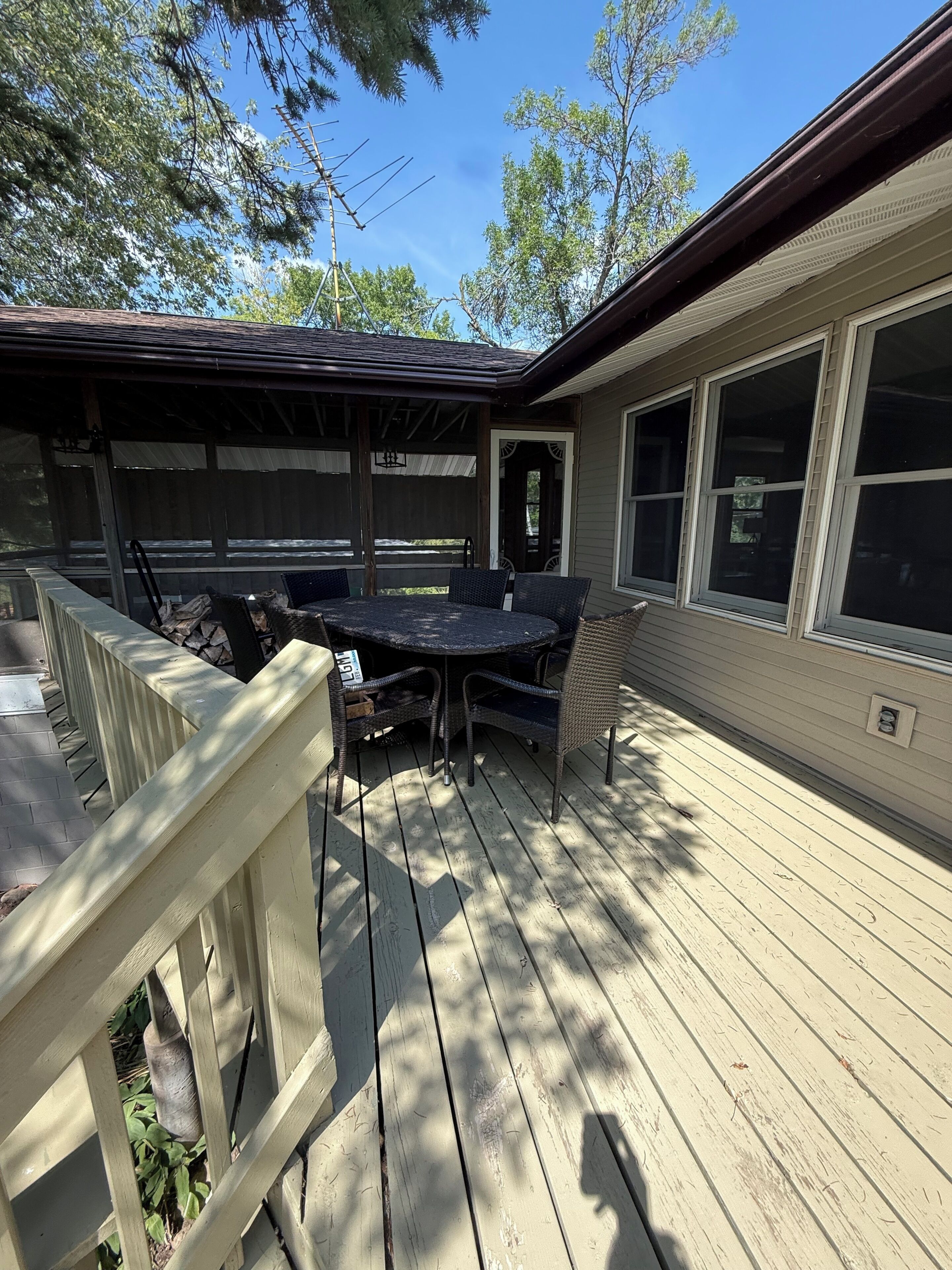 A covered patio with a table and chairs, a wooden deck, and a house with large windows.