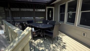 A covered patio with a table and chairs, a wooden deck, and a house with large windows.