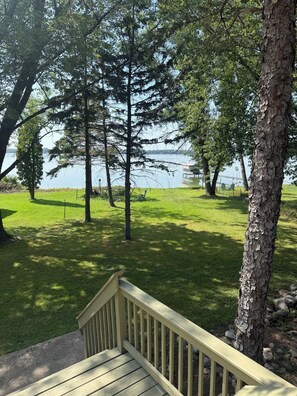 A wooden deck with a railing overlooking a grassy area with trees and a body of water in the background. - Rush Lake Retreat -plenty of room to sleep, even more room to unwind! (Rush City)
