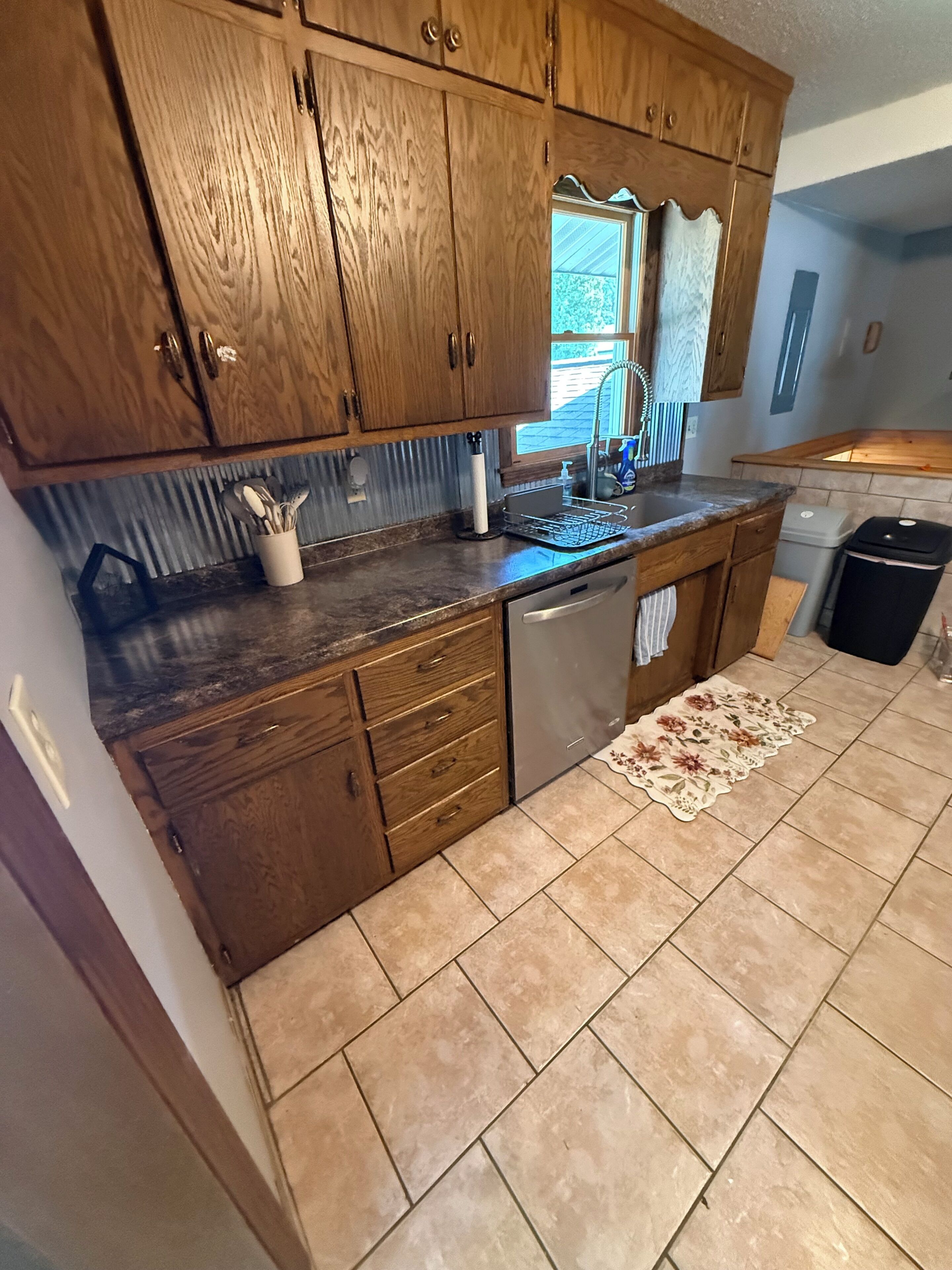 A kitchen with wooden cabinets, a dishwasher, and a tiled floor.