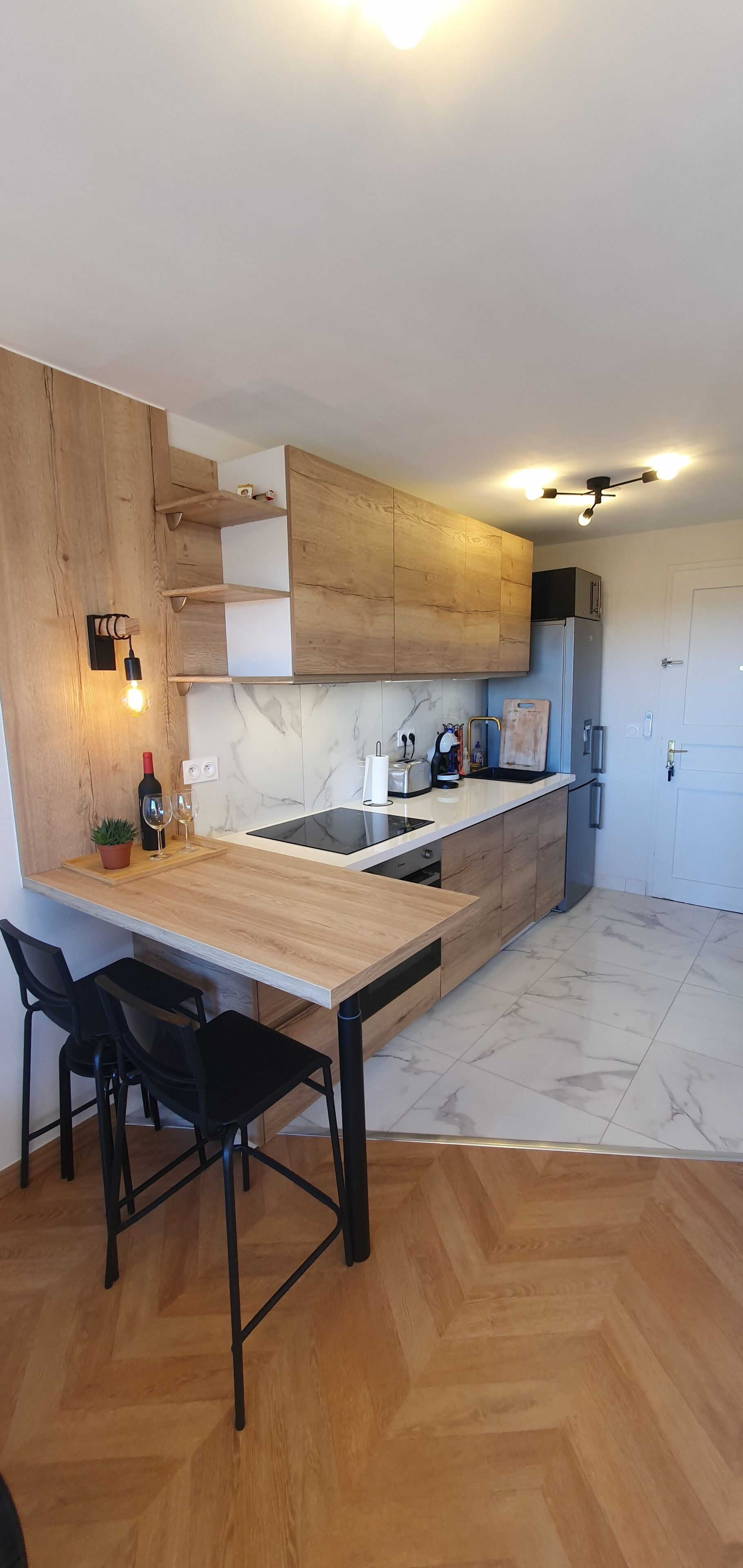 Une cuisine moderne avec des meubles en bois, une cuisinière encastrée et un coin repas doté de chaises noires.