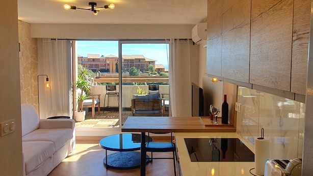 A modern kitchen with a dining area, large windows, and a view of the outdoors.