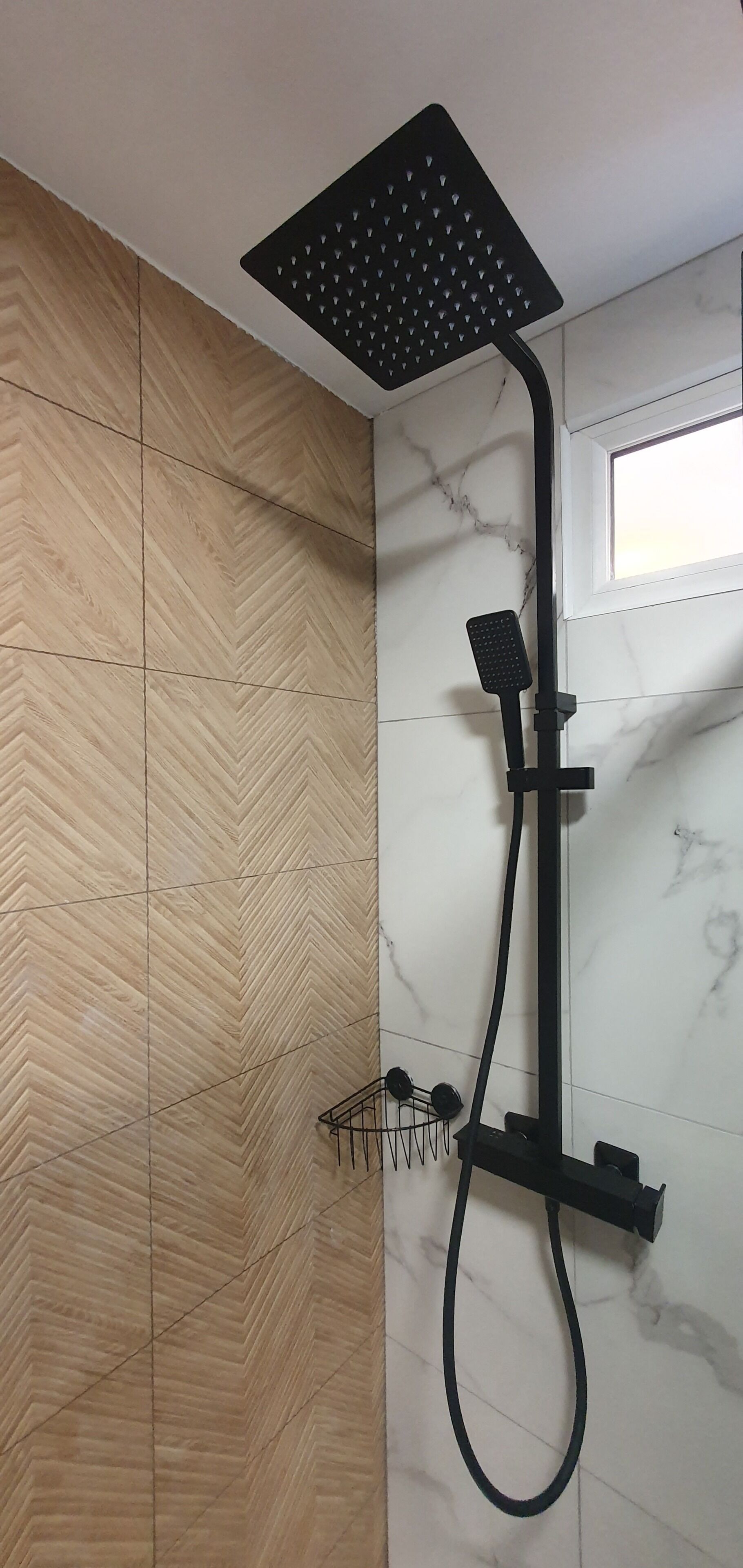 Douche met een vierkante douchekop en een handdouche, bevestigd aan een wand met een herringbone patroon en een marmeren gedeelte.