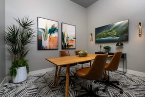 A modern dining area with a wooden table, four chairs, abstract paintings, a large TV, and a potted plant.