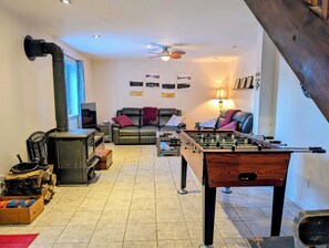 Un salon chaleureux avec une cheminée, des canapés, une table de baby-foot et un ventilateur de plafond.