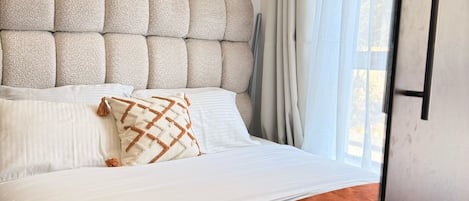 Una habitación de hotel con cama, almohadas, cabecero, cortinas y una ventana.