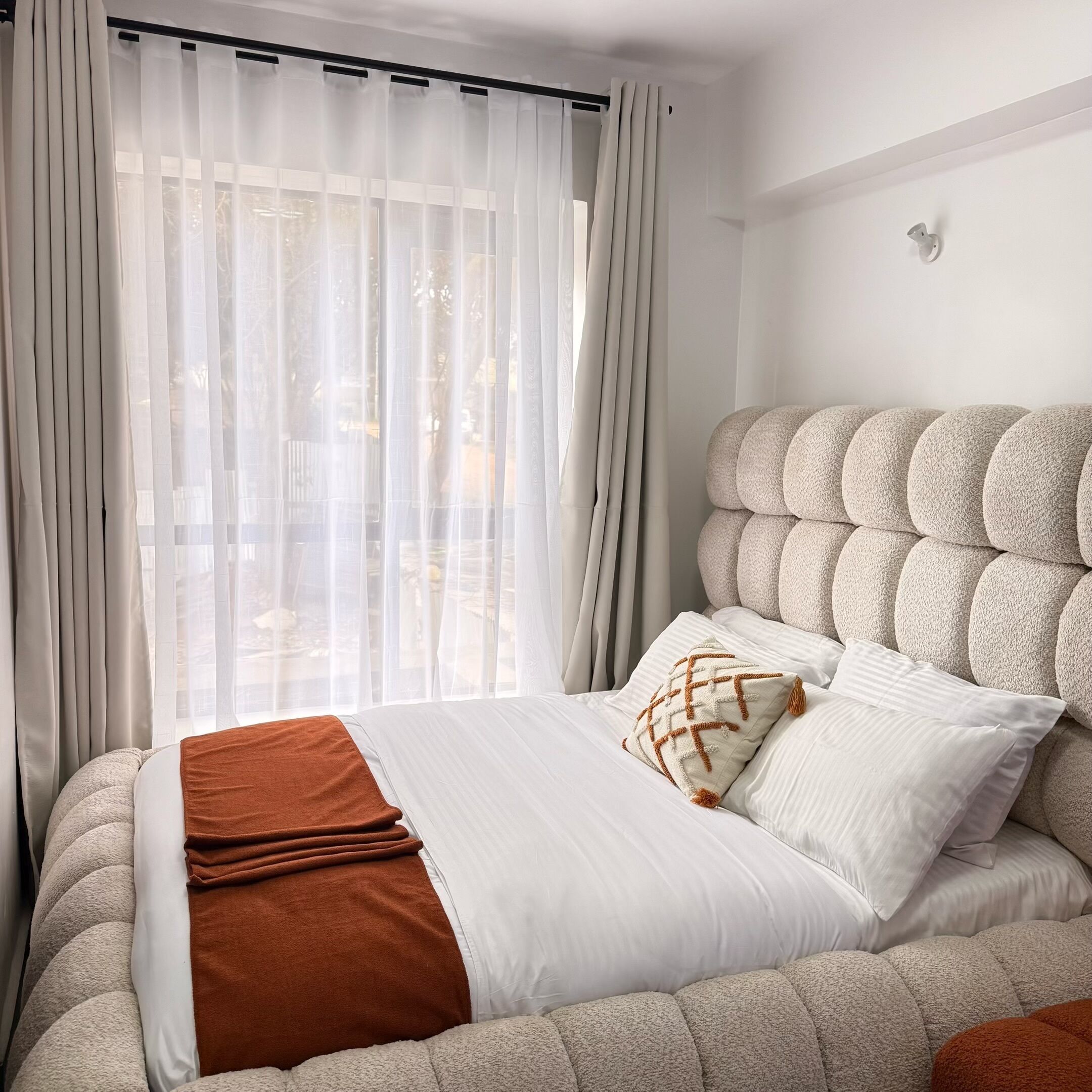 A bed with a tufted headboard, white bedding, and a brown throw blanket.
