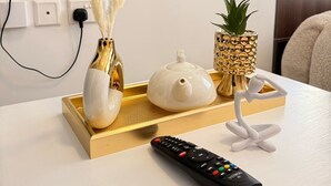 A white table with a gold tray holding a white teapot, two white vases with golden stems, a pineapple, and a black remote control. - Cozy studio bed & breakfast in quaint Nairobi with 
swimming pool (Nairobi)