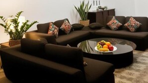 Una sala moderna con un sofá seccional, una mesa de centro redonda con fruta y un ventilador de techo.