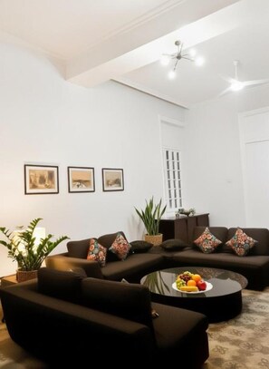 A modern living room with a sectional sofa, a round coffee table with fruit, and a ceiling fan. - Stunning specious luxury apartment high ceiling (Cairo Governorate)