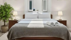Un dormitorio con cama, lámparas de noche, una ventana y una planta en maceta.