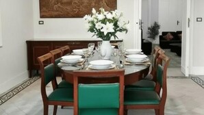 Comedor con una mesa redonda dispuesta para seis personas, rodeada de sillas tapizadas en verde.