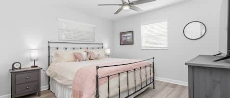 Un dormitorio con cama, mesitas de noche, ventilador de techo, espejo adosado a la pared y ventana con persianas.