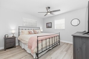 Een slaapkamer met een bed, nachtkastjes, een plafondventilator, een spiegel aan de muur en een raam met zonwering.