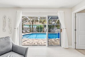 Ein Zimmer mit einer Schiebetür zum Poolbereich, einem grauen Sofa und einer weißen Tür.