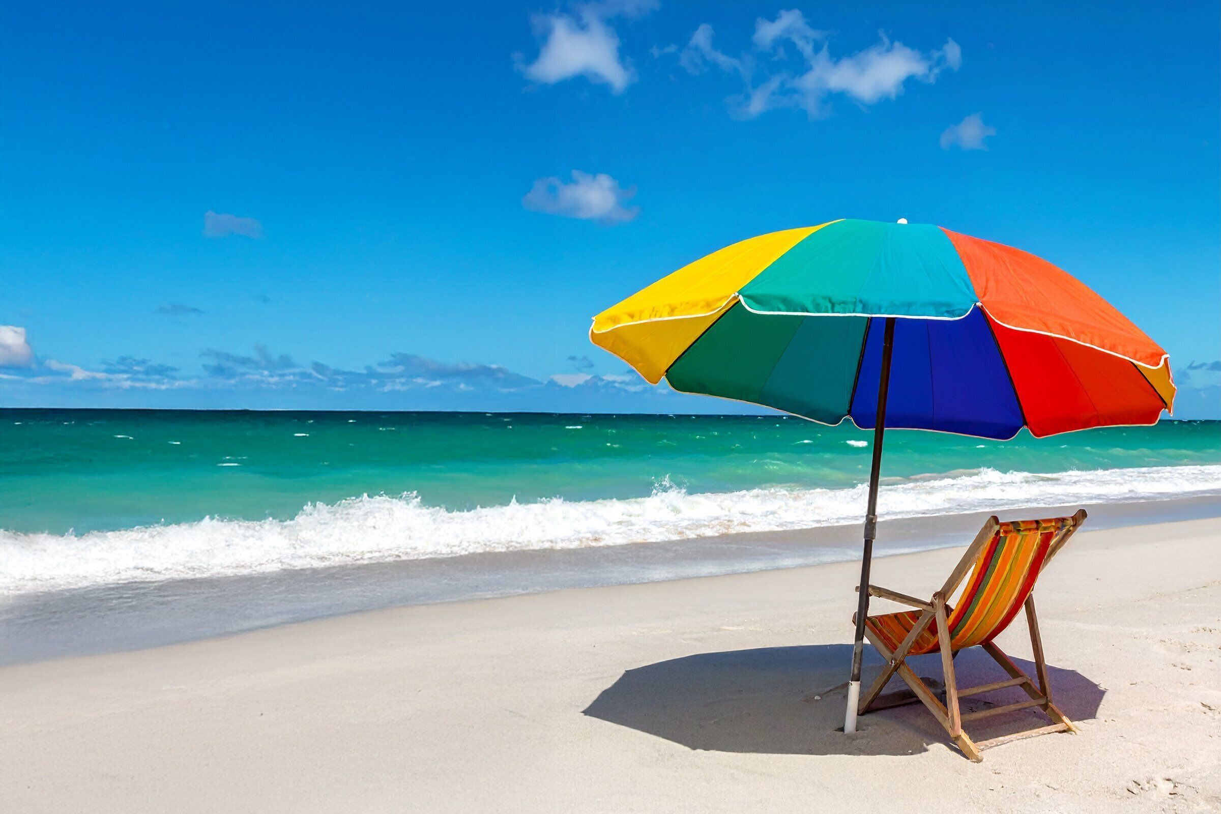 En badestrand med en farverig parasol og en strandstol.