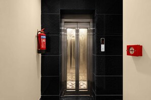 An elevator with a fire extinguisher mounted on the wall to its left.