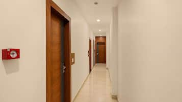 A corridor with wooden doors, a fire alarm, and a clean tiled floor.