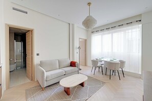 A modern living room with a sofa, a coffee table, a dining area with chairs, and a large window with curtains. - Modern a/c - 1bdr/4p Flat - Montorgueil (Paris)
