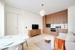 A modern living space with a dining area, a kitchen with wooden cabinets, a flat-screen TV, and a sofa. - Modern a/c - 1bdr/4p Flat - Montorgueil (Paris)